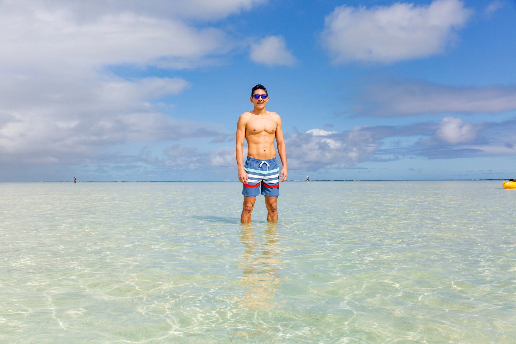 A man standing in calm, clear shallow water with an island behind him