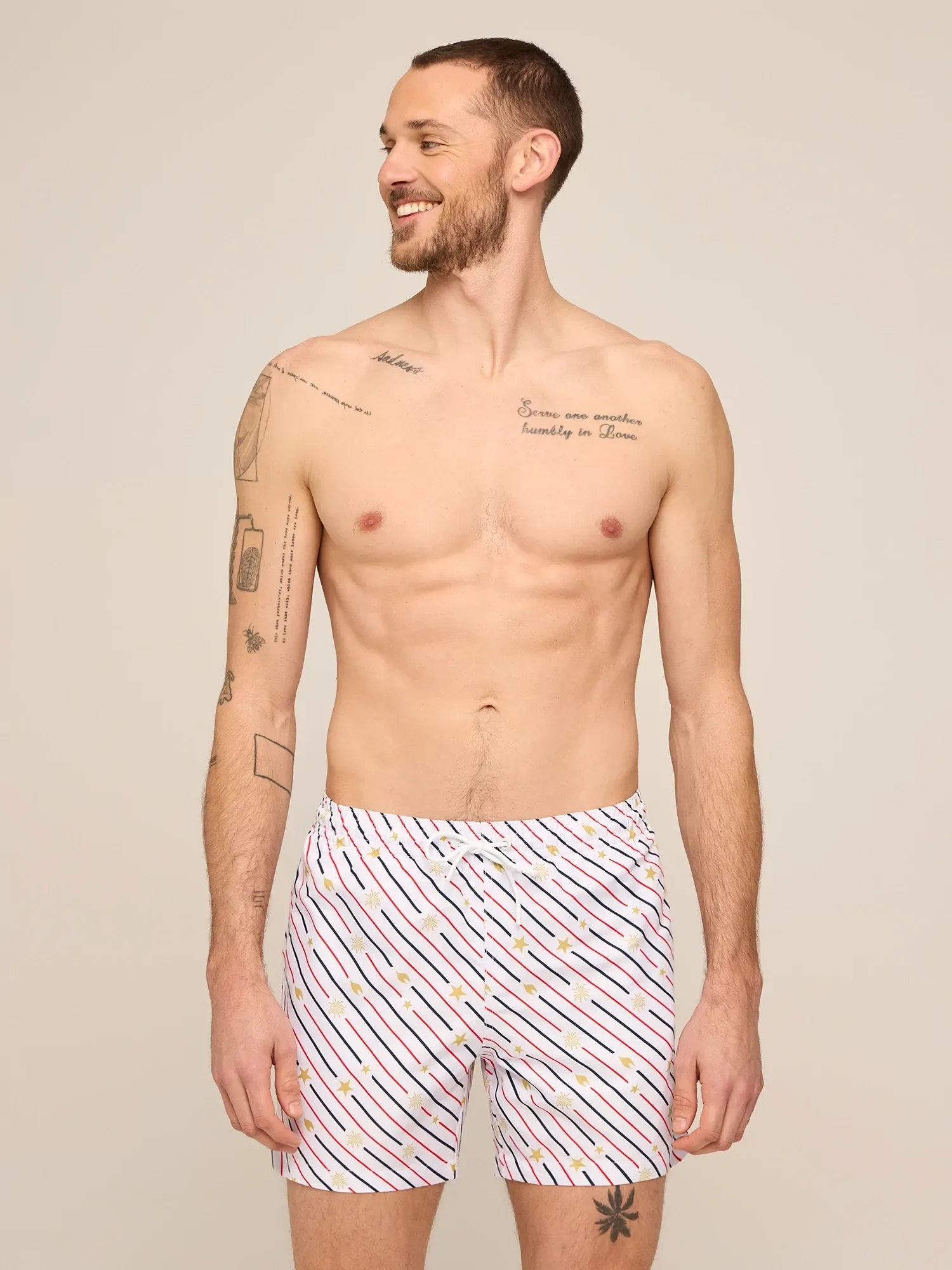 A shirtless man in white swim trunks with a red and navy print
